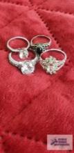 Four silver colored gemstone rings, three have clear gemstones, one has marking of U with an arrow
