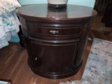 (UPBR2) OVAL WOODEN SIDE TABLE WITH SINGLE DRAWER AND CABINET. IT MEASURES 26"W X 20"D X 25-1/2"T.